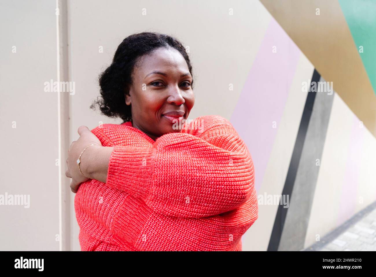 Lächelnde Frau trägt einen orangefarbenen Pullover, der sich umarmt Stockfoto