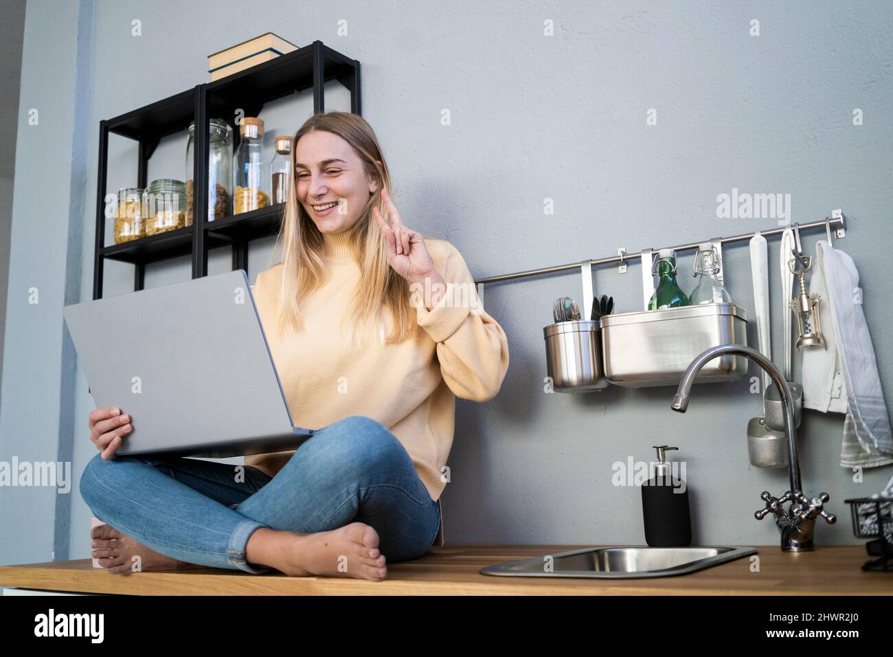 Glückliche Frau, die zu Hause bei einem Videoanruf über einen Laptop eine Friedensgeste macht Stockfoto