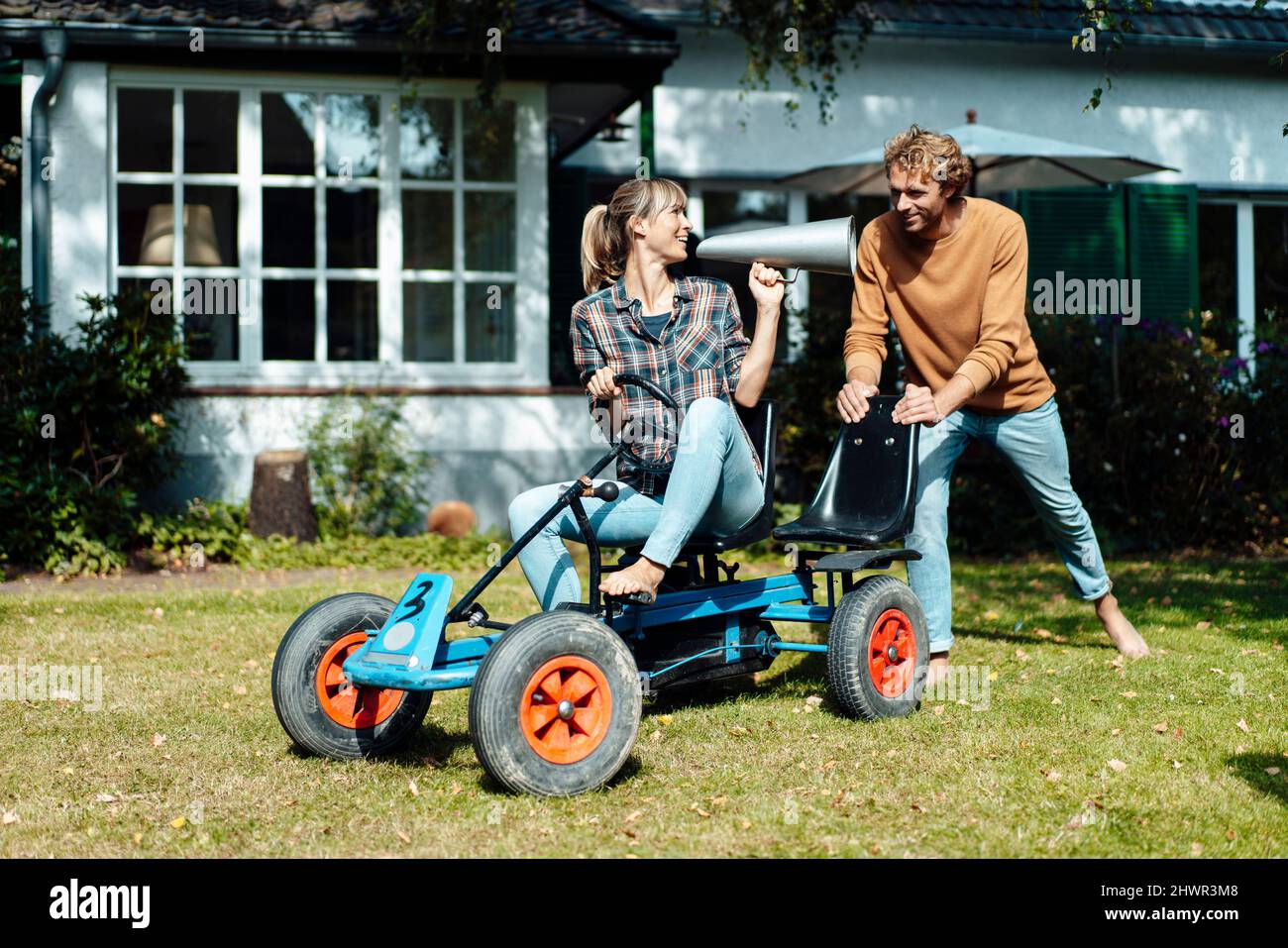Mann schiebt Frau auf Go-Kart durch Megaphon im Garten reden Stockfoto