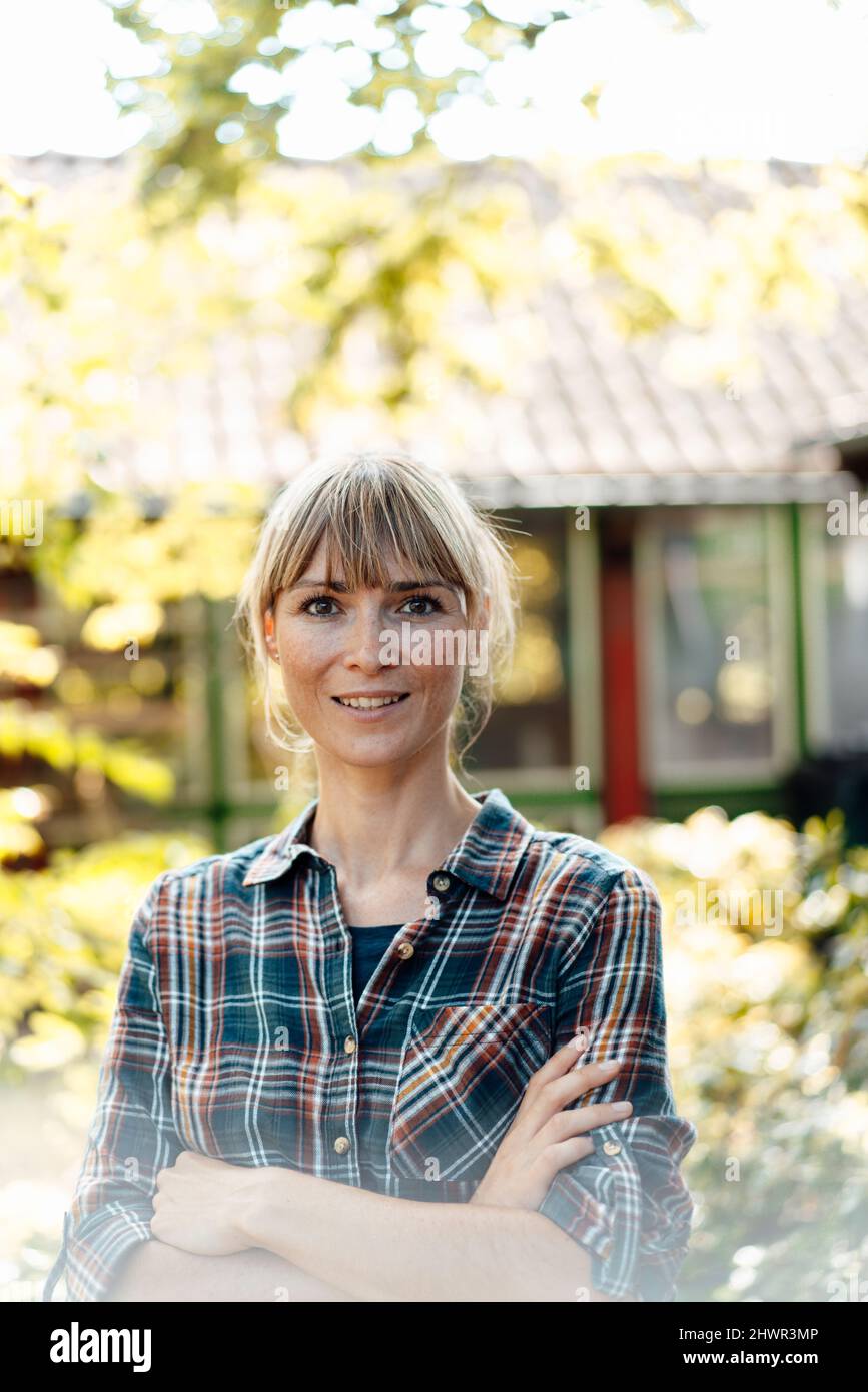 Kontemplative Frau mit gekreuzten Armen im Garten Stockfoto