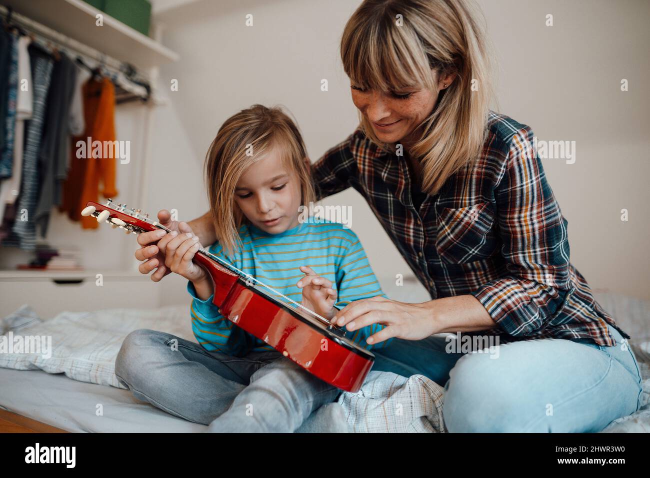 Mutter lehrt Sohn Gitarre spielen im Schlafzimmer zu Hause Stockfoto