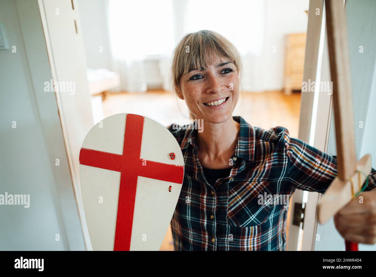 Lächelnde Frau mit Schwert und Schild zu Hause Stockfoto