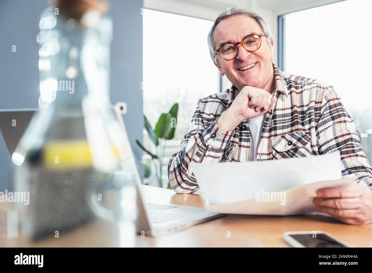 Glücklicher älterer Mann mit Brille, der mit der Geldrechnung am Tisch sitzt Stockfoto