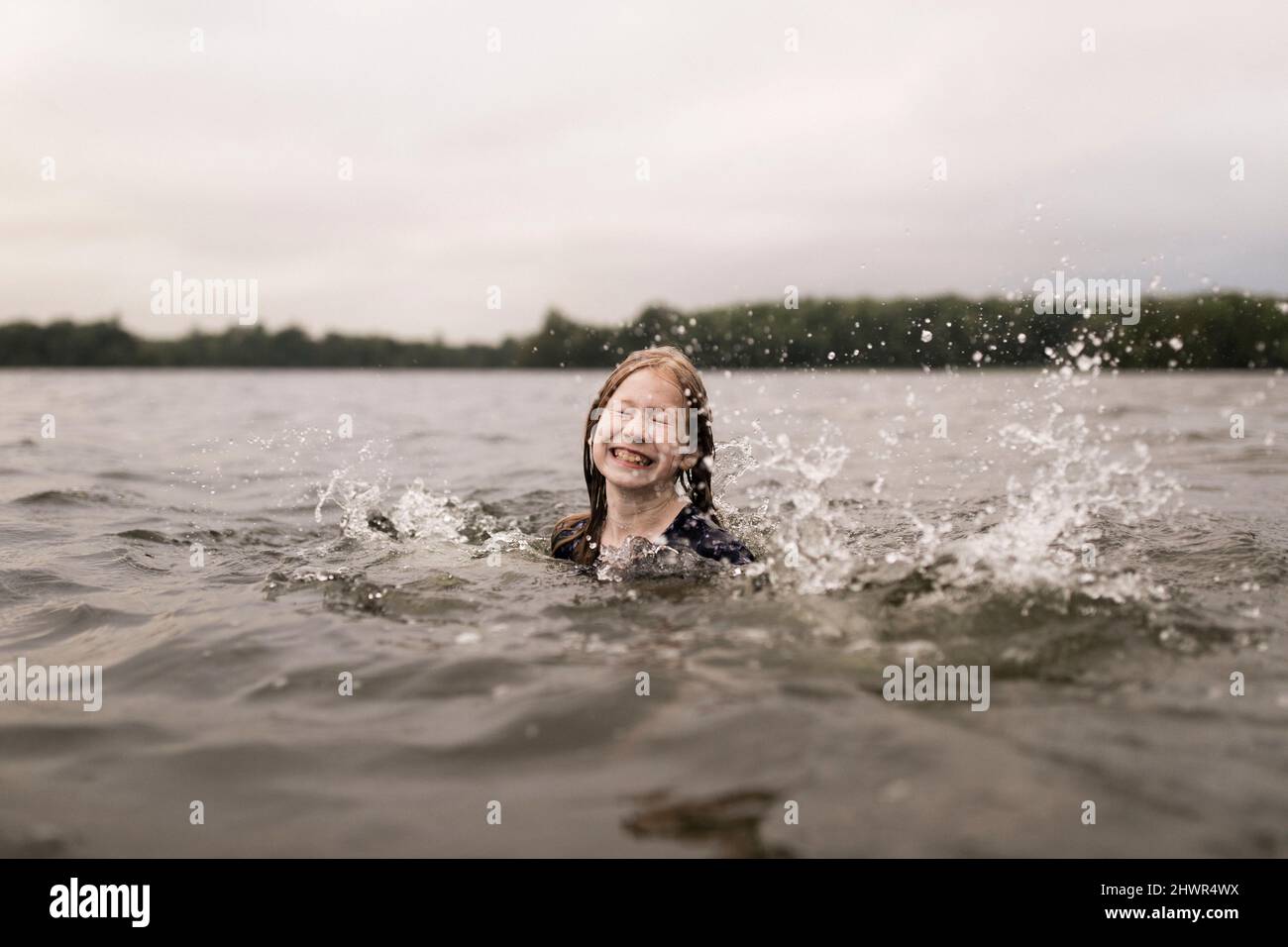Mädchen mit geschlossenen Augen spritzt mit Wasser im See Stockfoto