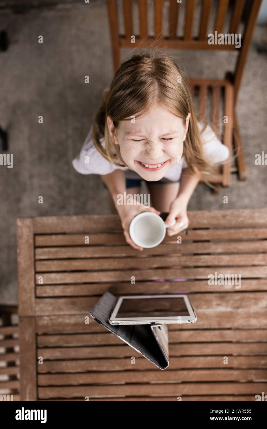 Lächelndes Mädchen mit Milchbecher und Tablet-PC auf dem Tisch Stockfoto