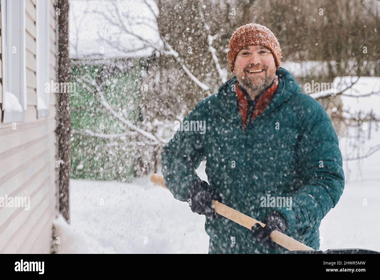 Mann mit Schneeschaufel, der im verschneiten Garten steht Stockfoto