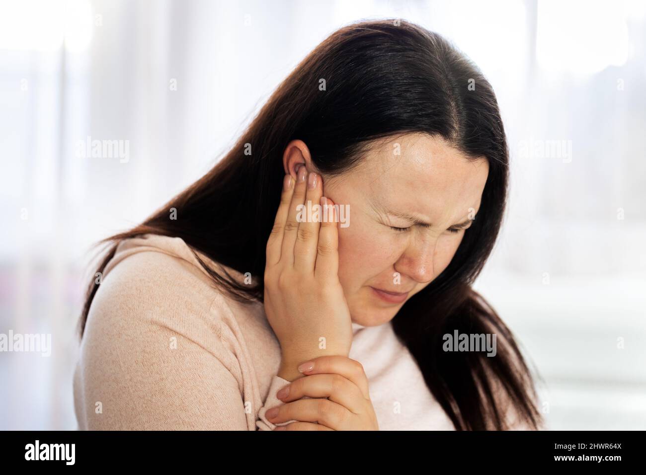 Junge Frau mit starken Ohrenschmerzen und Tinnitus nach COVID-19, Ohrerkrankungen, Gesundheitskonzept Stockfoto