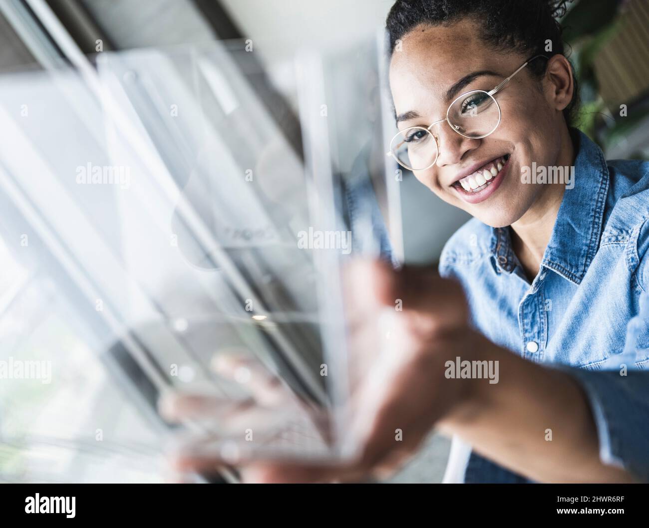 Lächelnde Geschäftsfrau analysiert Glasoobjekt im Büro Stockfoto