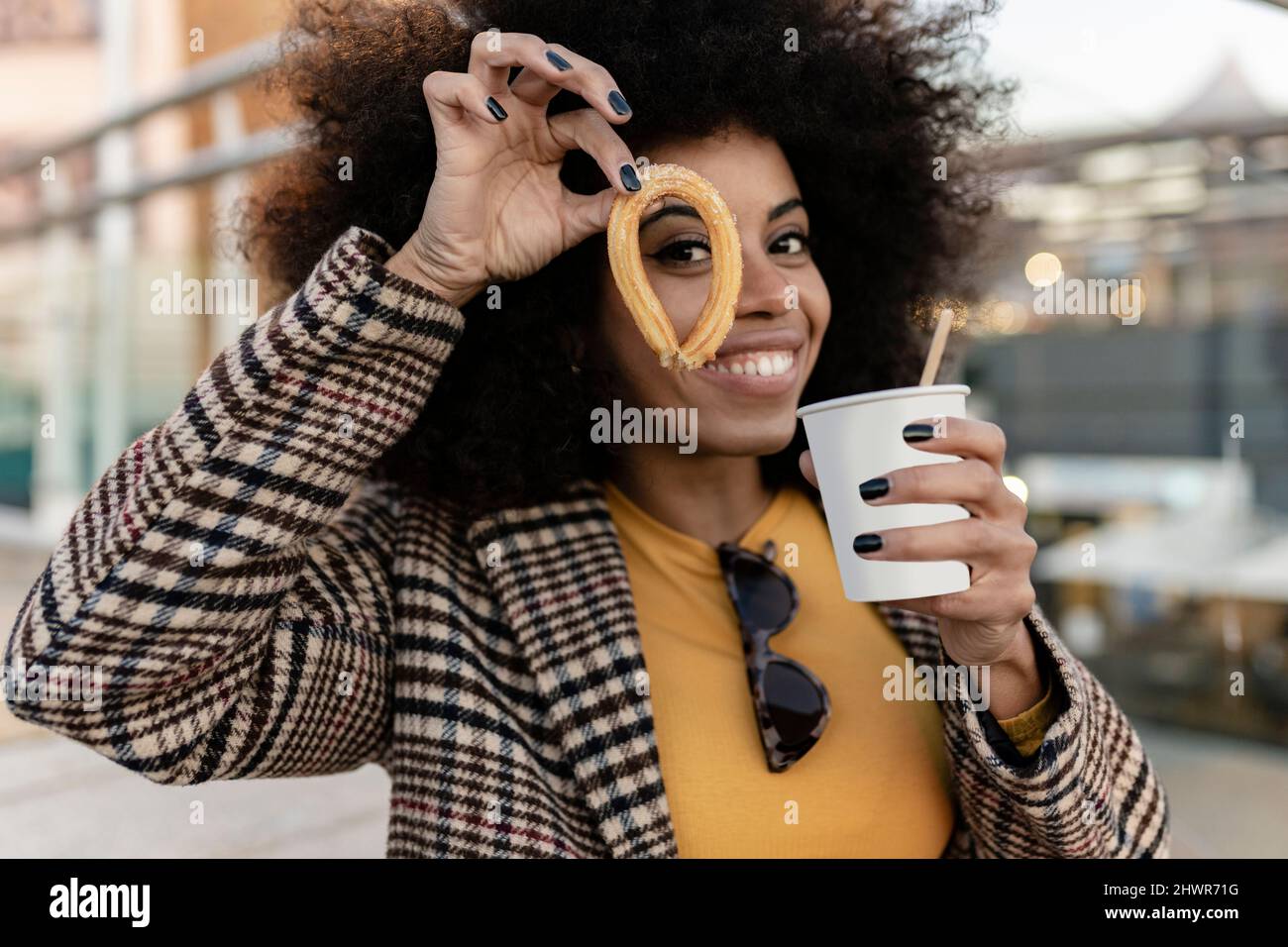Lächelnde Frau mit Churro mit Einweg-Tasse Stockfoto
