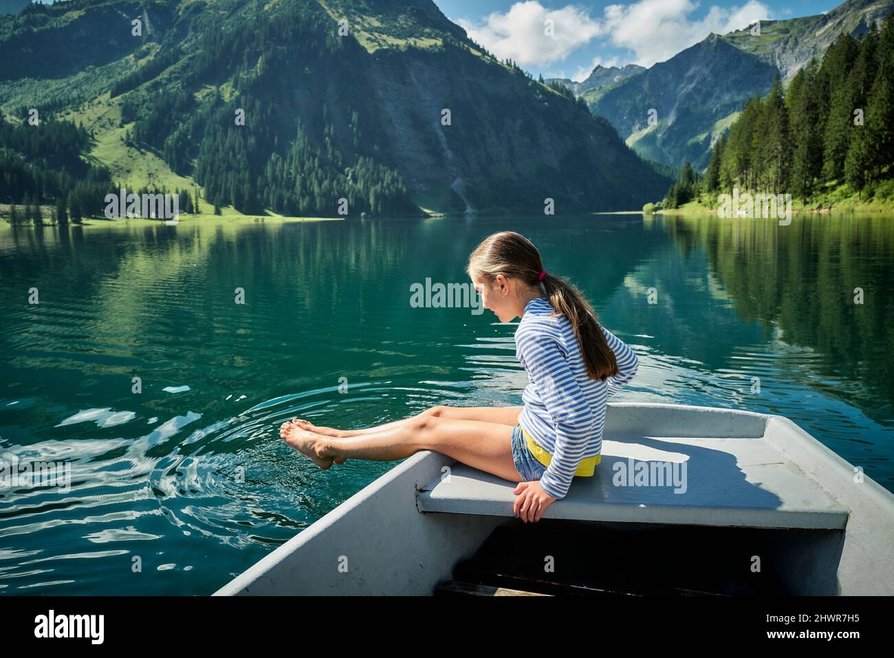 Mädchen, das auf dem Bug des Ruderbootes sitzt und die Füße in den See taucht Stockfoto