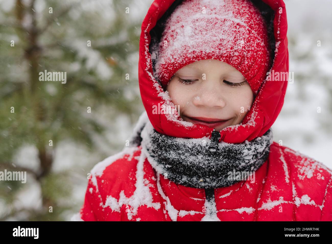 Lächelnder Junge mit Schnee auf Strickmütze und warmer Kleidung im Winter Stockfoto