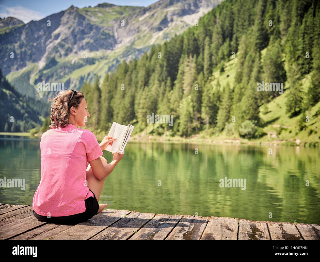 Frau mit Buchtag träumte auf dem Steg am See Stockfoto