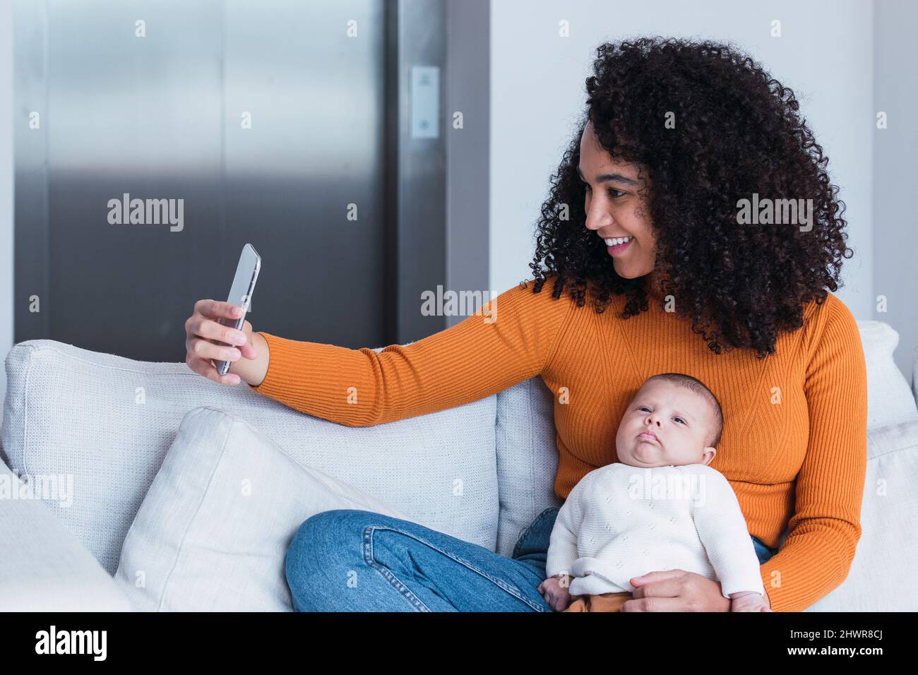 Mutter mit Baby Junge Selfie auf Smartphone im Wohnzimmer Stockfoto