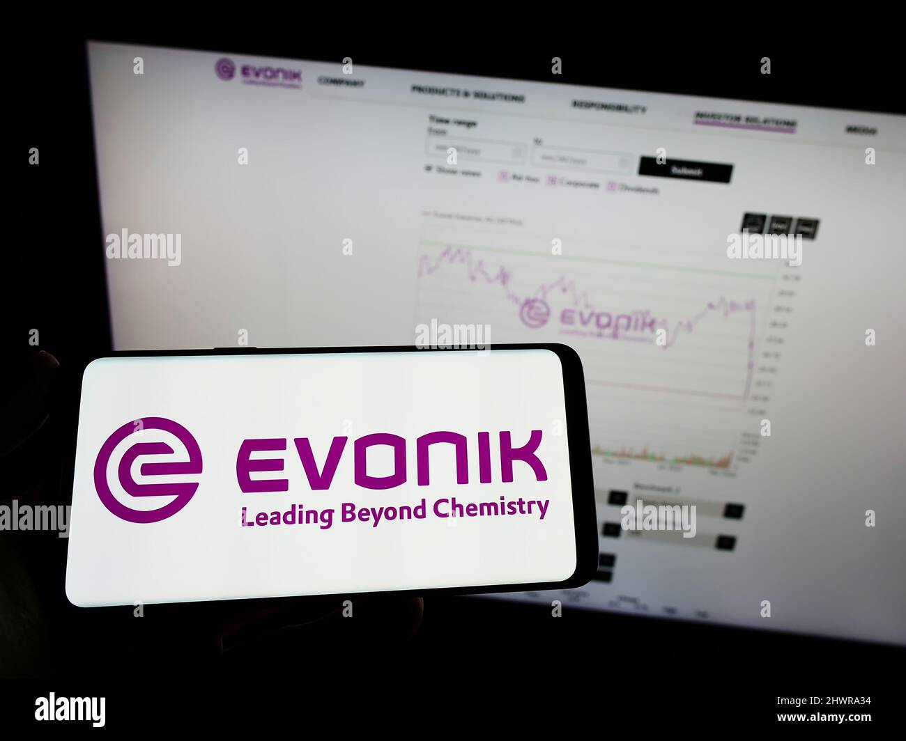 Person mit Mobiltelefon und Logo des deutschen Chemiekonzerns Evonik Industries AG auf dem Bildschirm vor der Webseite. Konzentrieren Sie sich auf die Telefonanzeige. Stockfoto