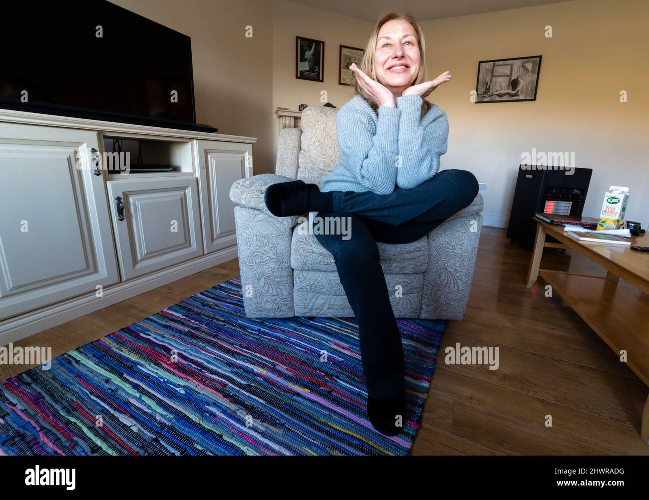Große blonde Frau macht morgens Dehnübungen im Sessel Stockfoto