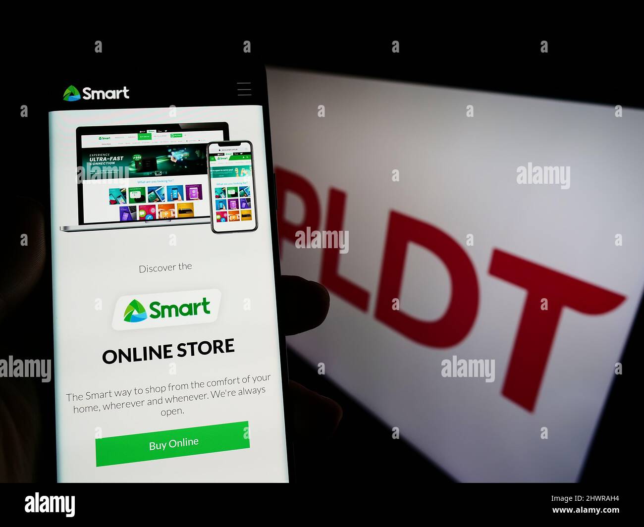 Person mit Mobiltelefon und Webseite des philippinischen Telekommunikationsunternehmens PLDT Inc. Auf dem Bildschirm mit Logo. Fokusmitte von auf dem Telefon-Display. Stockfoto