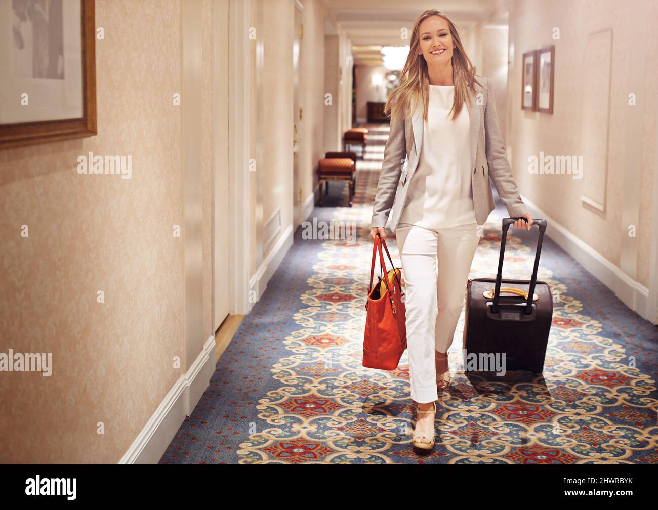 Ich übernachte nur im Besten. Aufnahme einer Frau, die mit einem Koffer den Flur eines Hotels entlang läuft. Stockfoto