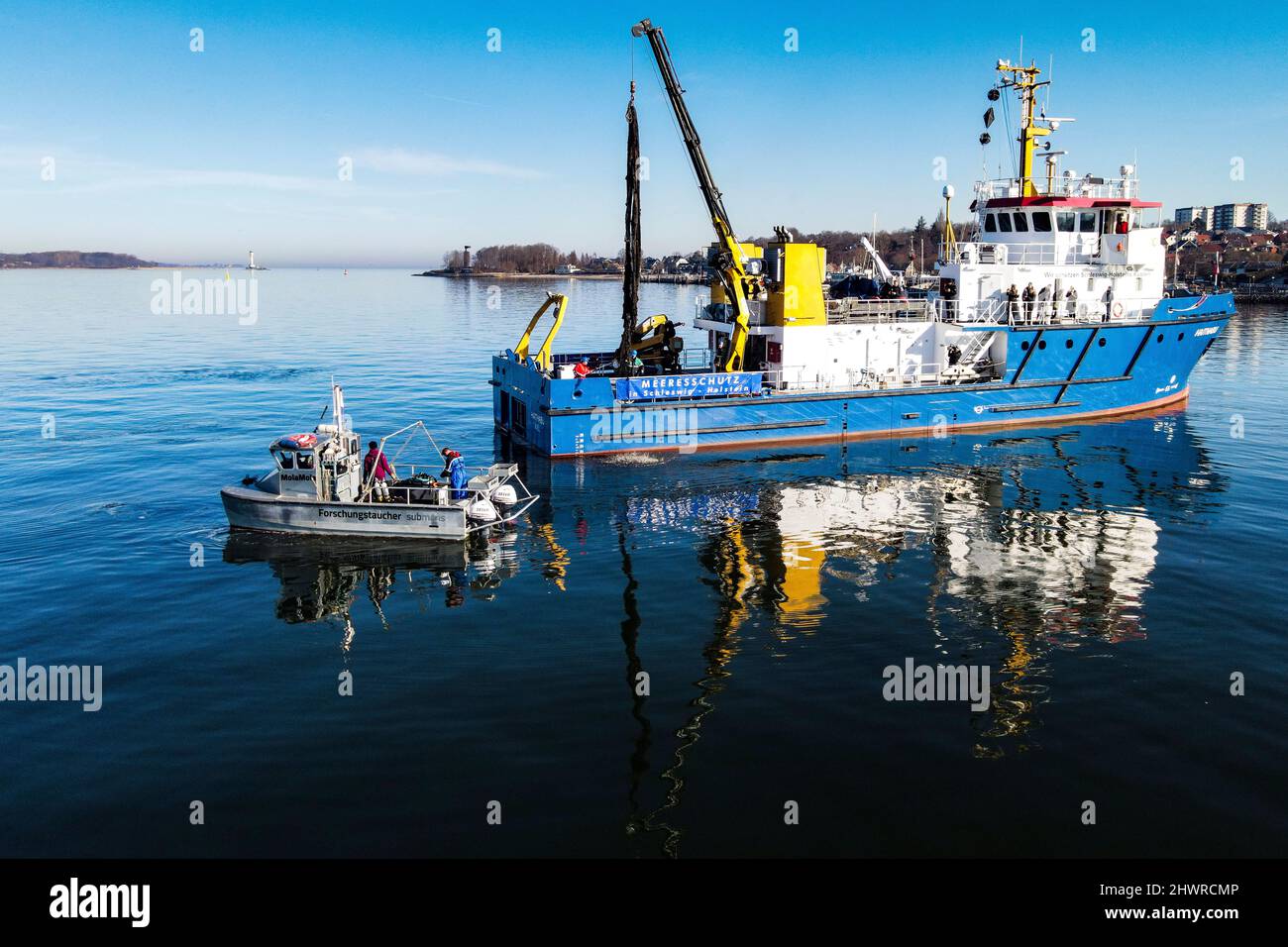 Kiel, Deutschland. 07. März 2022. Eine verlorene Fischfalle wird mit einem Kran an Bord des Forschungsschiffs MS Haithabu gebracht (Drohnenbild). Gemeinsam mit dem Schleswig-holsteinischen Umweltministerium hat die Umweltstiftung WWF am 07.03.2022 diese verlorene Fischfalle in der Ostsee vor Kiel zurückgewonnen. Die sogenannten Geisternetze stellen eine Gefahr für Fische und Seevögel dar. Sie können auch zu Todesfallen für Robben und Schweinswale werden, wenn die Tiere in ihnen gefangen werden. Quelle: Frank Molter/dpa/Alamy Live News Stockfoto