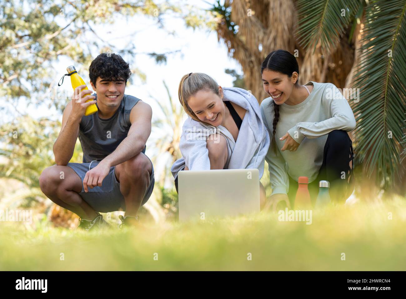 Drei junge Sportbegeisterte schauen sich den Laptop an und lachen im Park Stockfoto