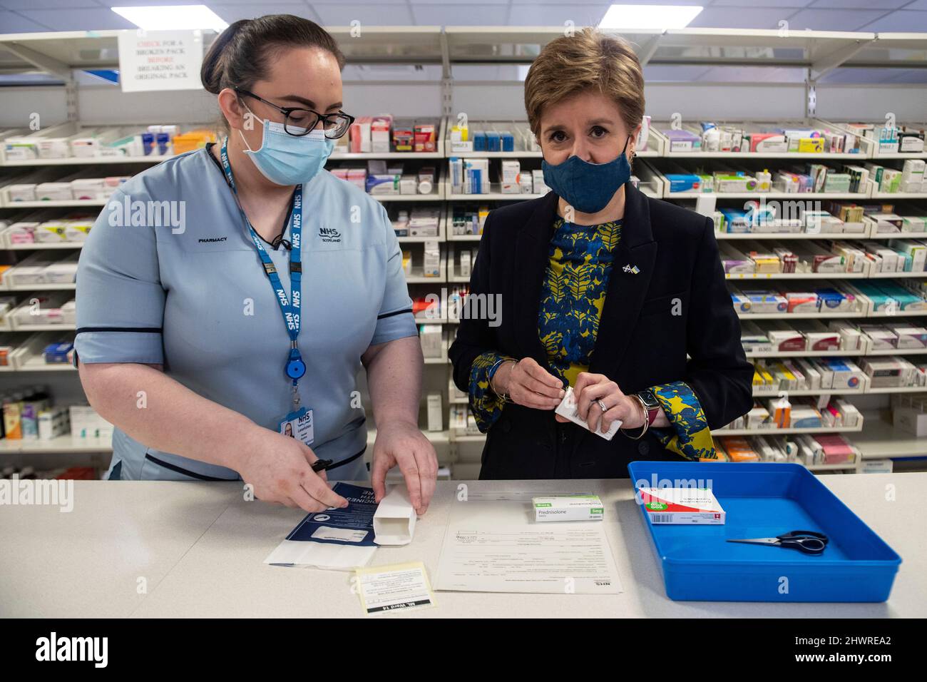 Die erste Ministerin Schottlands, Nicola Sturgeon (rechts), spricht mit einem Angestellten der Pharmazie am Monklands University Hospital in Airdrie in North Lanarkshire, Schottland, während der schottischen Lehrwoche. Bilddatum: Montag, 7. März 2022. Stockfoto