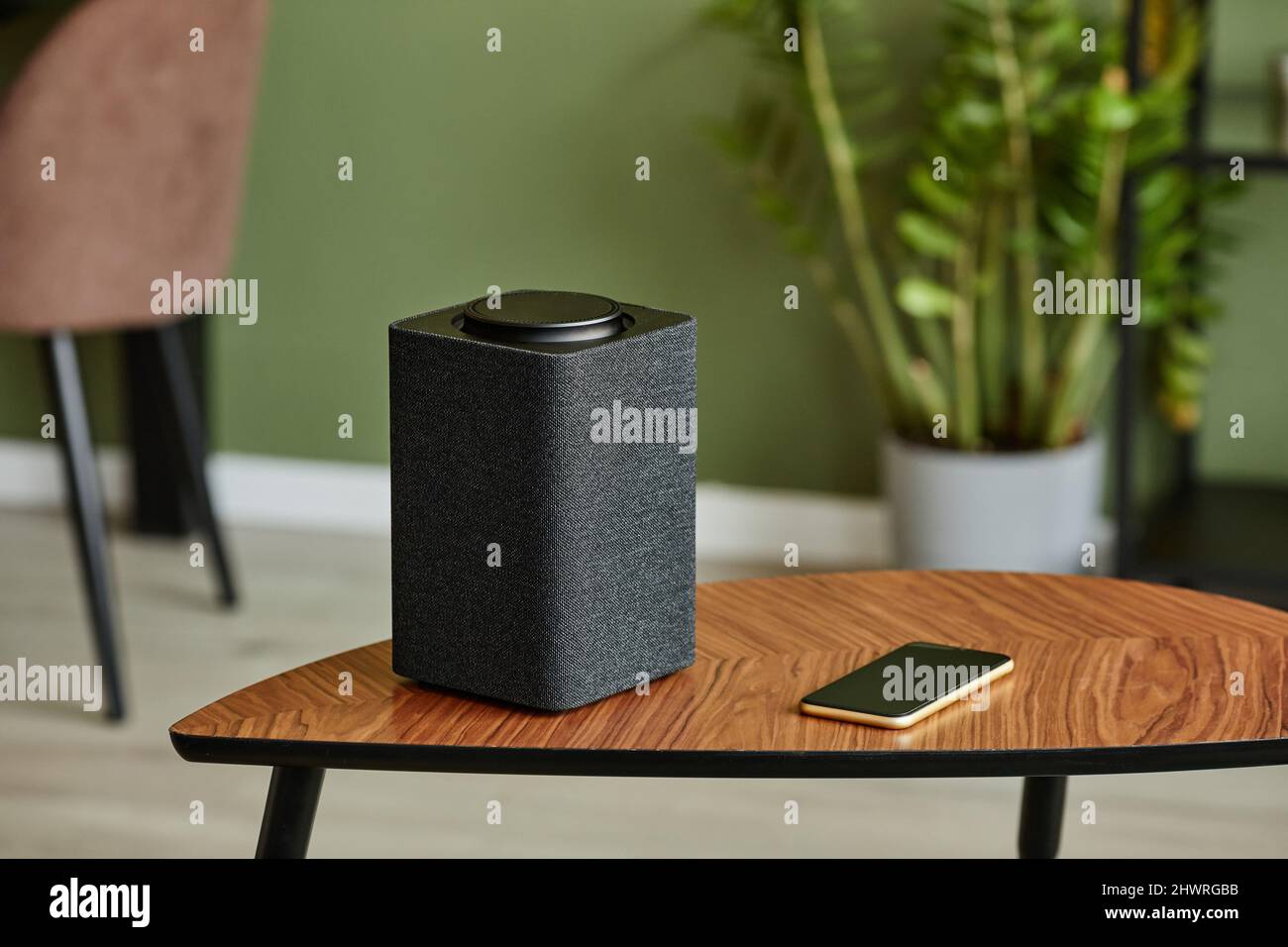 Minimales Hintergrundbild von Smart Speaker mit Home AI-System auf Holztisch gegen grüne Wand, Kopierplatz Stockfoto