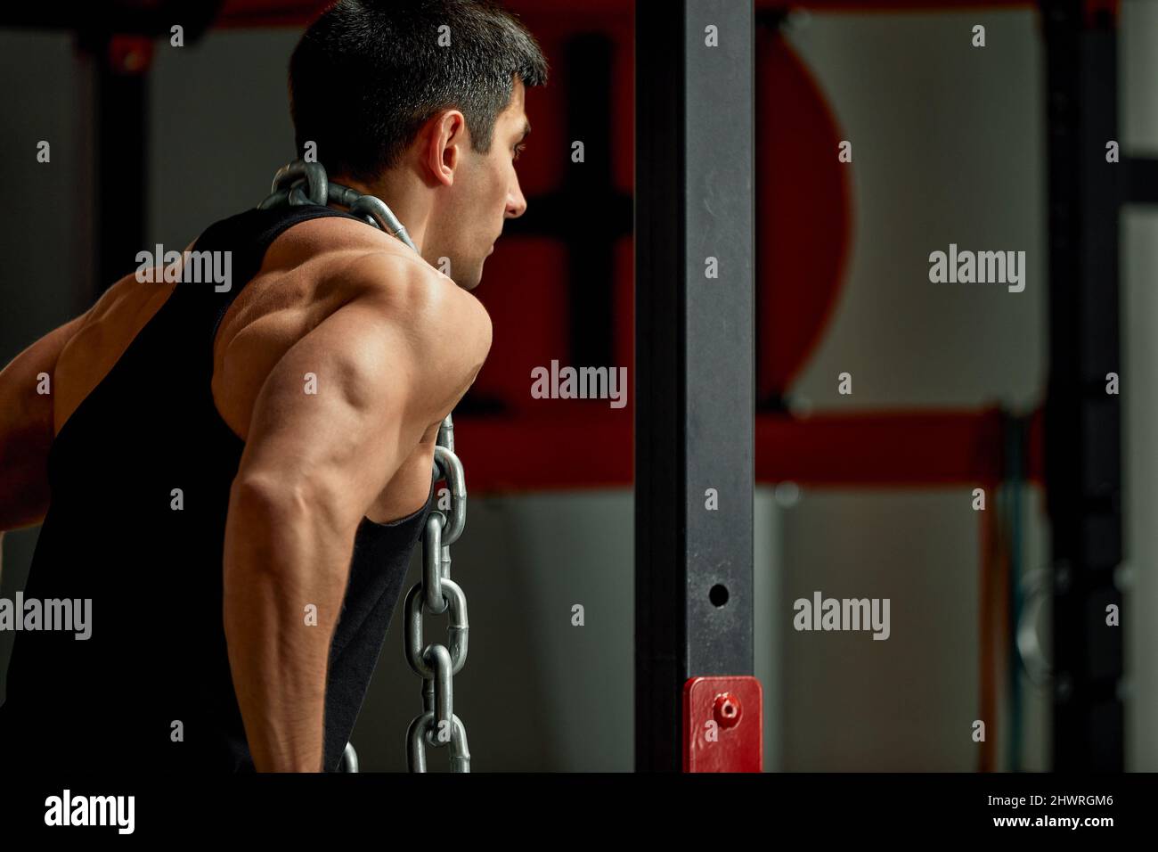 Arbeiten Sie mit eigenem Gewicht, der Athlet macht Übungen auf den unebenen Balken mit einer Kette um den Hals. Stockfoto