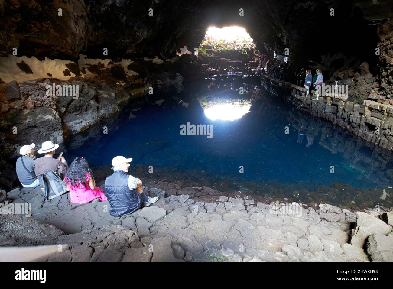 Touristen sitzen am Rand des Lavatunnels mit Salzwasser-Lagunen-See in jameos del agua lanzarote, kanarische Inseln, spanien die weißen Flecken sind die einzigartigen blin Stockfoto