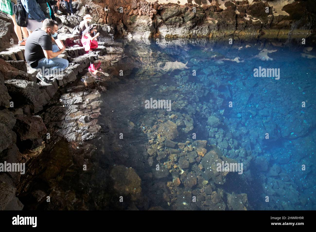 Touristen sitzen am Rand des Lavatunnels mit Salzwasser-Lagunen-See in jameos del agua lanzarote, kanarische Inseln, spanien die weißen Flecken sind die einzigartigen blin Stockfoto