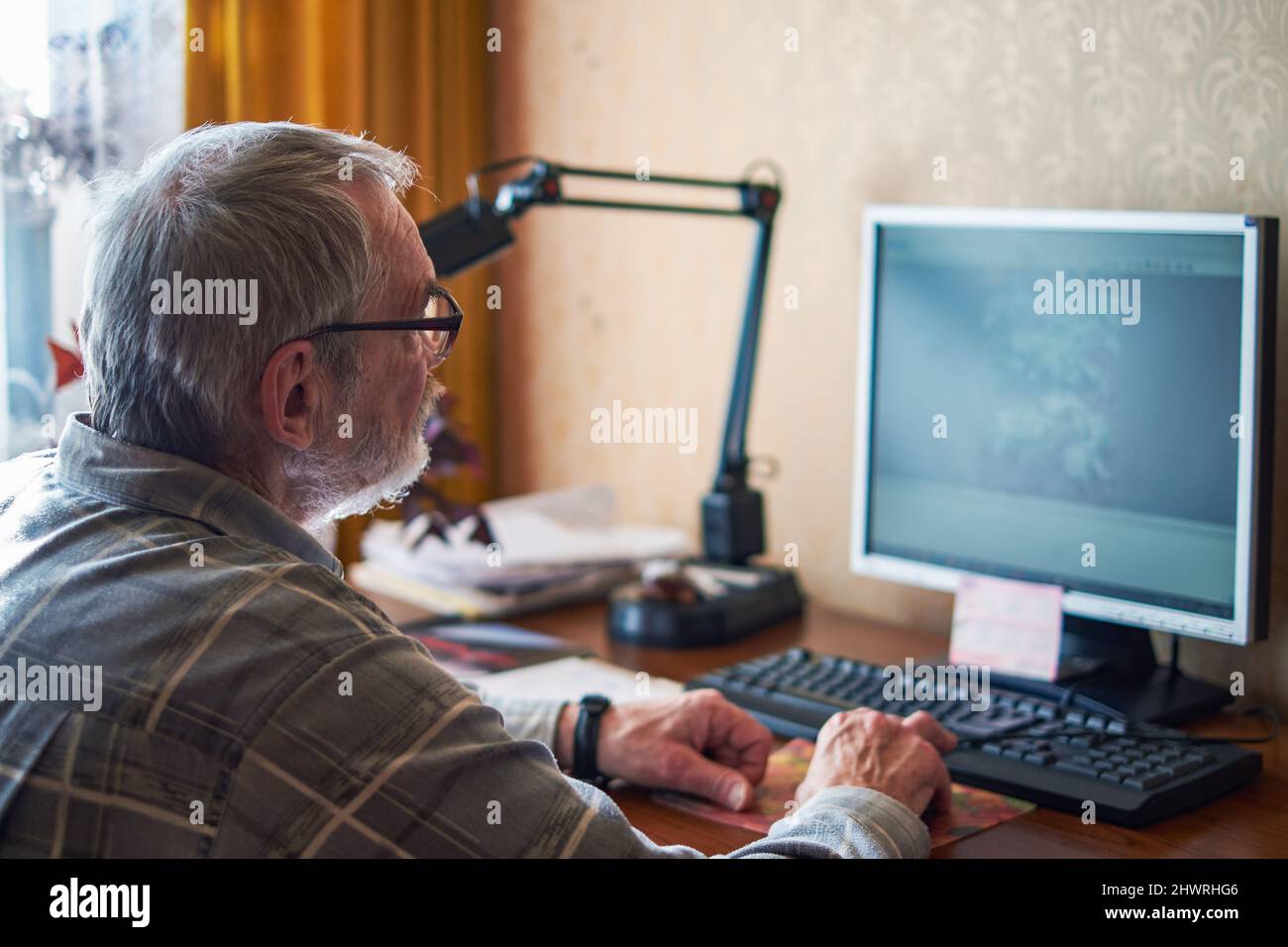 Ein älterer Mann, über 70, arbeitet zu Hause an einem Computer Stockfoto