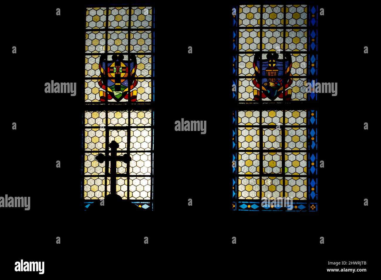 Das katholische Kreuz auf der Spitze des Beichtstuhls vor dem Hintergrund eines sonnendurchfluteten Buntglasfensters. Das Foto wurde in der Kirche aufgenommen. Stockfoto