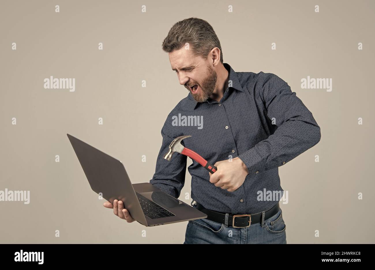 Wütender Mann schlug Laptop-Computer mit Hammer grauen Hintergrund, Absturz Stockfoto
