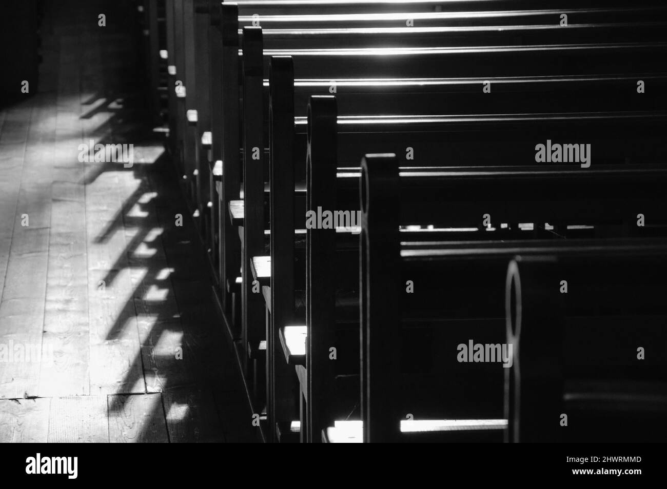 Reihen von Kirchenbänken. Sonnenlicht filterte durch das Buntglasfenster. Selektiver Fokus. Historisches Foto in Schwarzweiß Stockfoto