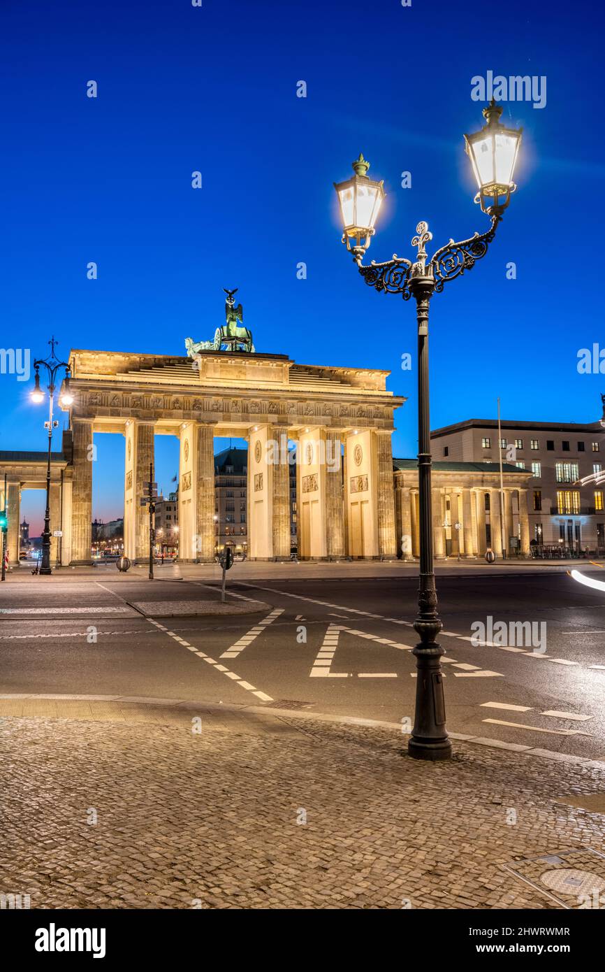 Die Rückseite des beleuchteten Brandenburger Tors in Berlin mit einer historischen Straßenbeleuchtung im Morgengrauen Stockfoto