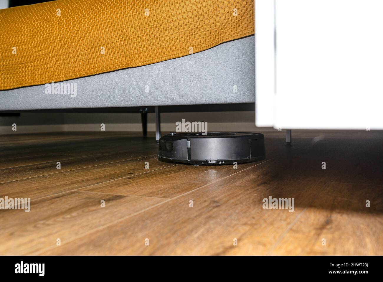 Ein moderner Roboter-Staubsauger reinigt Vinylplatten unter Schlafzimmermöbeln, einen autonomen Reinigungsroboter. Stockfoto