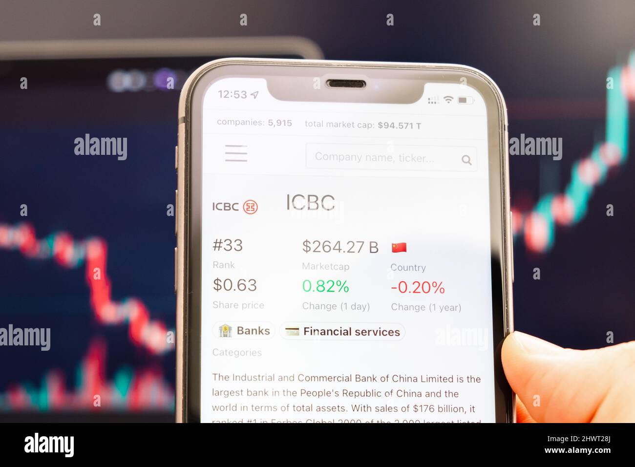 ICBC-Aktienkurs auf dem Bildschirm des Mobiltelefons in mans Hand mit wechselnden Börsengraphen im Hintergrund, Februar 2022, San Francisco, USA. Stockfoto