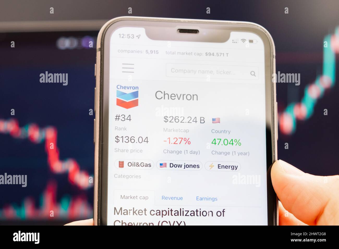 Chevron-Aktienkurs auf dem Bildschirm des Mobiltelefons in mans-Hand mit wechselnden Börsengraphen im Hintergrund, 2022. Februar, San Francisco, USA. Stockfoto