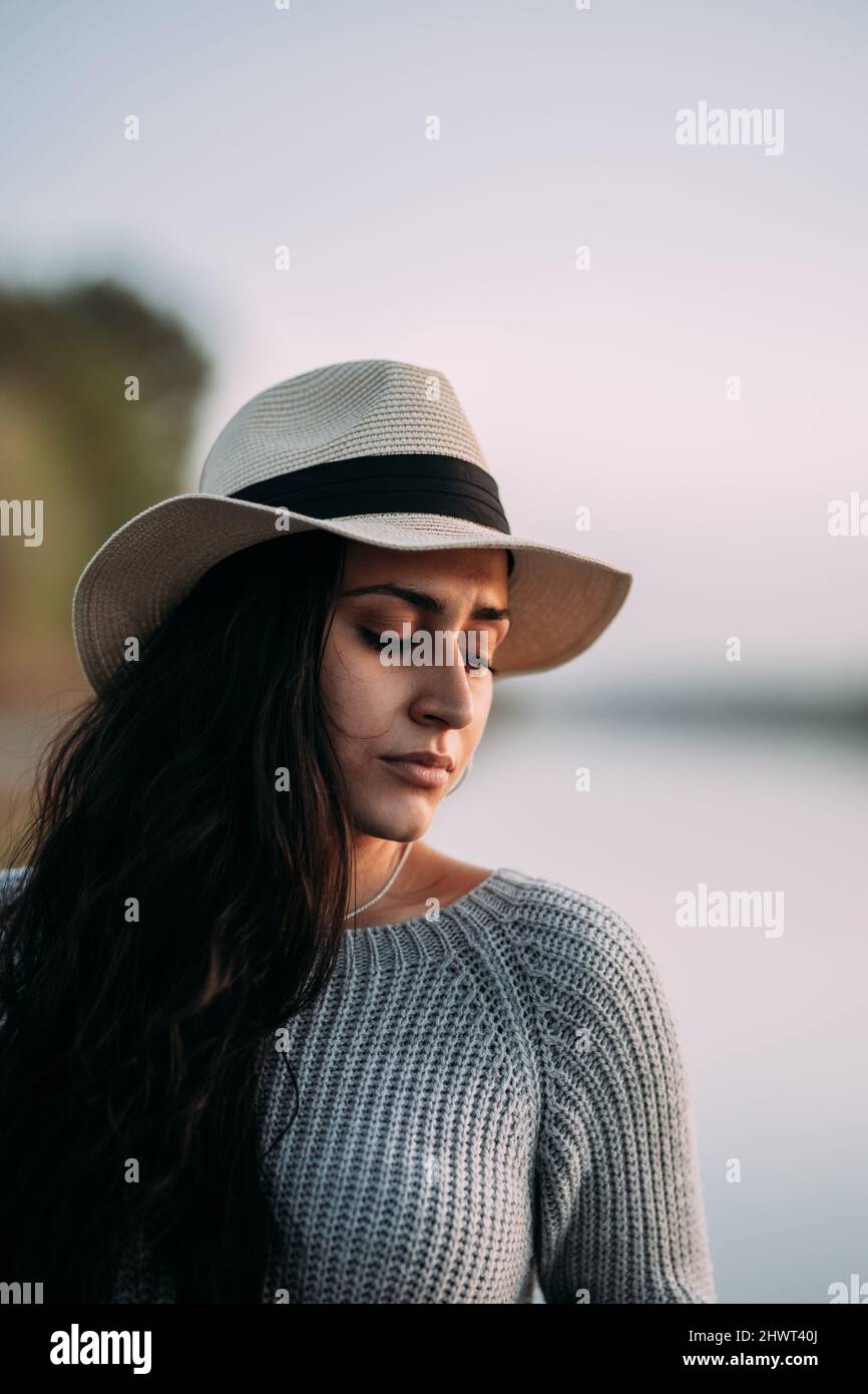 Porträt einer nachdenklichen und ernsten Frau mit geschlossenen Augen und einem Hut am See Stockfoto