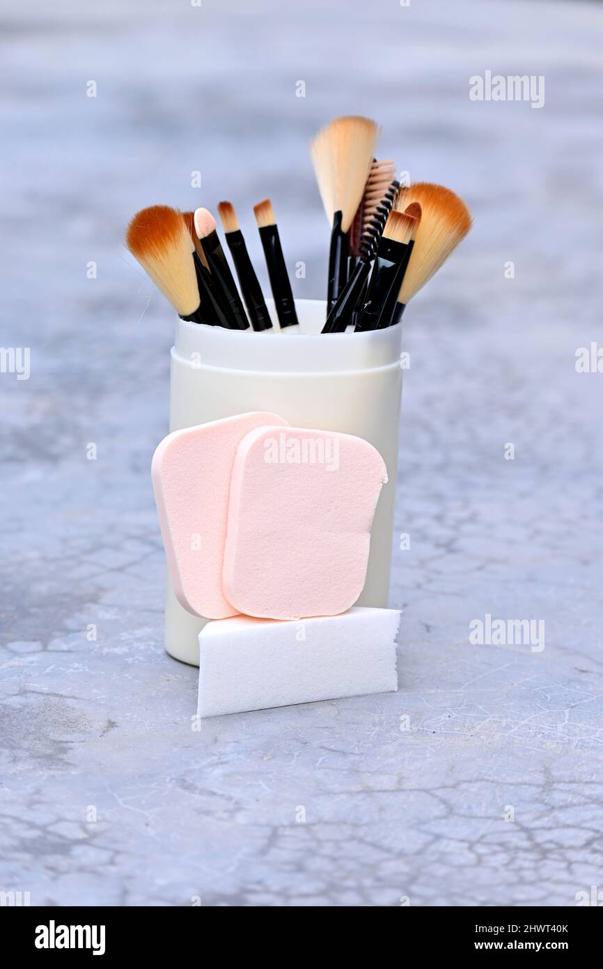 Nahaufnahme der Haufen weiß braun Make-up-Kit Pinsel mit Schwamm Ball in der Kunststoffbox über aus Fokus grau braunen Hintergrund. Stockfoto