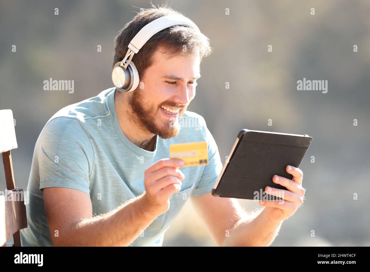 Glücklicher Mann mit Kopfhörern, der online Musik oder Videos mit einem Tablet und einer Kreditkarte kauft Stockfoto