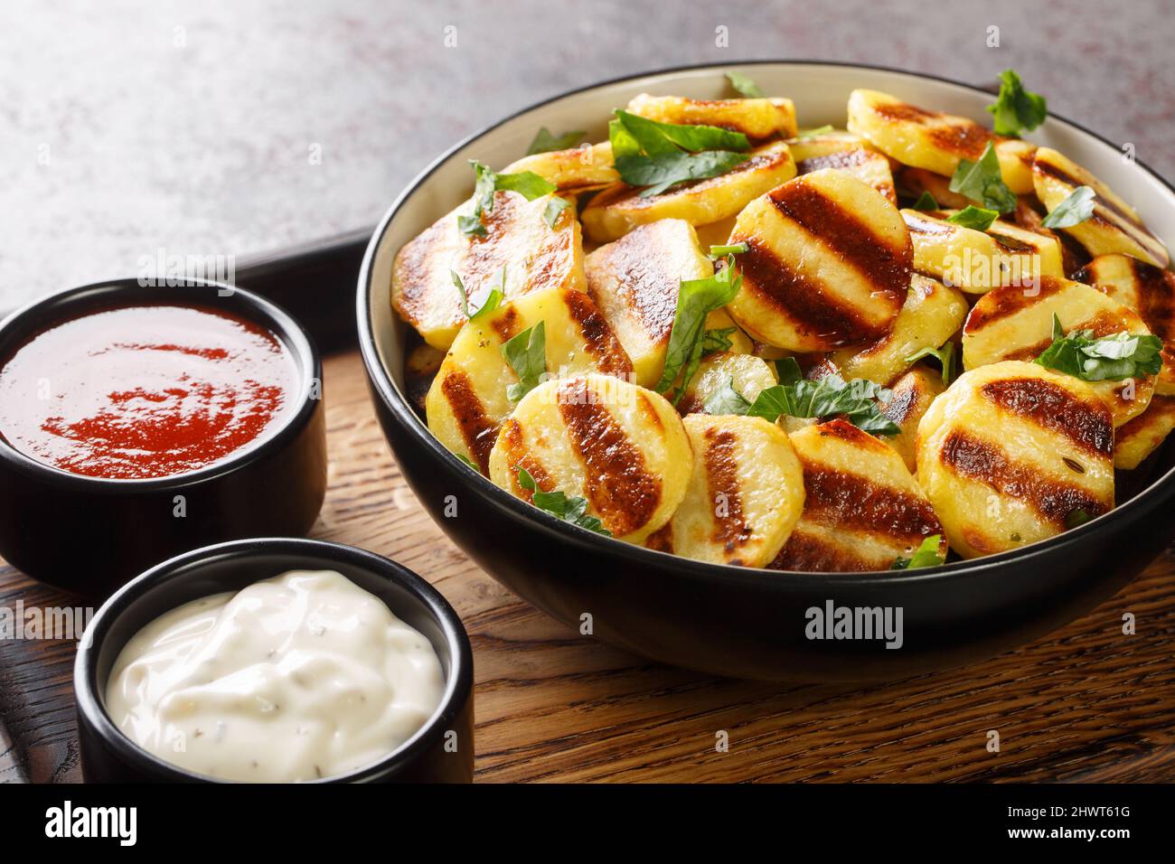 Gegrillte Kartoffeln mit Streifen und zwei Saucen in Nahaufnahme auf einem Holzbrett auf dem Tisch. Horizontal Stockfoto