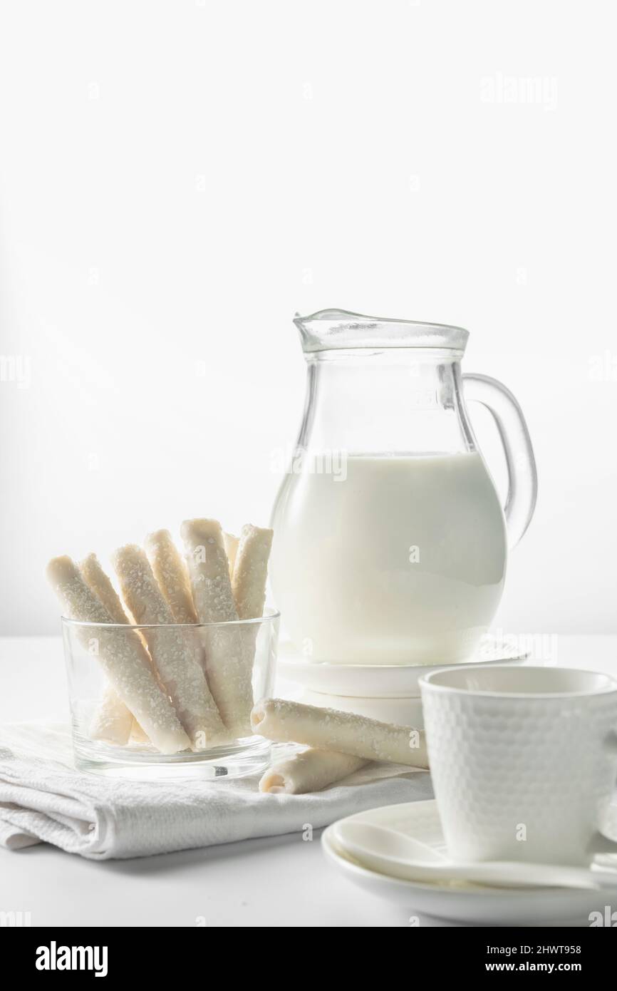 Kanne mit Milch und süßen Waffelbrötchen aus Kokosflocken Stockfoto