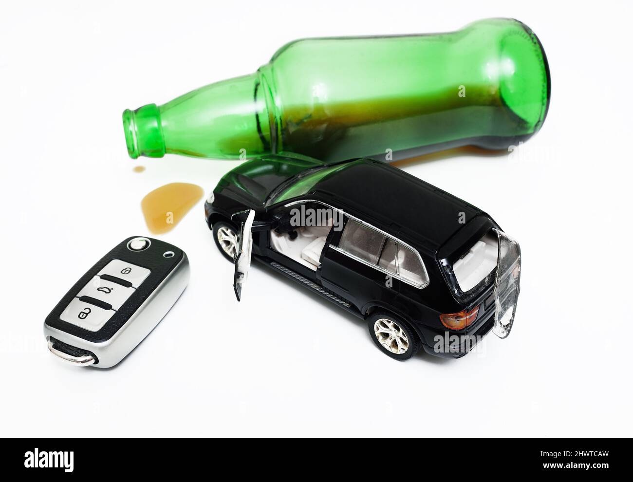 Ein zerbrochenes Spielzeugauto, eine Flasche mit Alkoholresten und ein Autoschlüssel auf weißem Hintergrund. Stockfoto