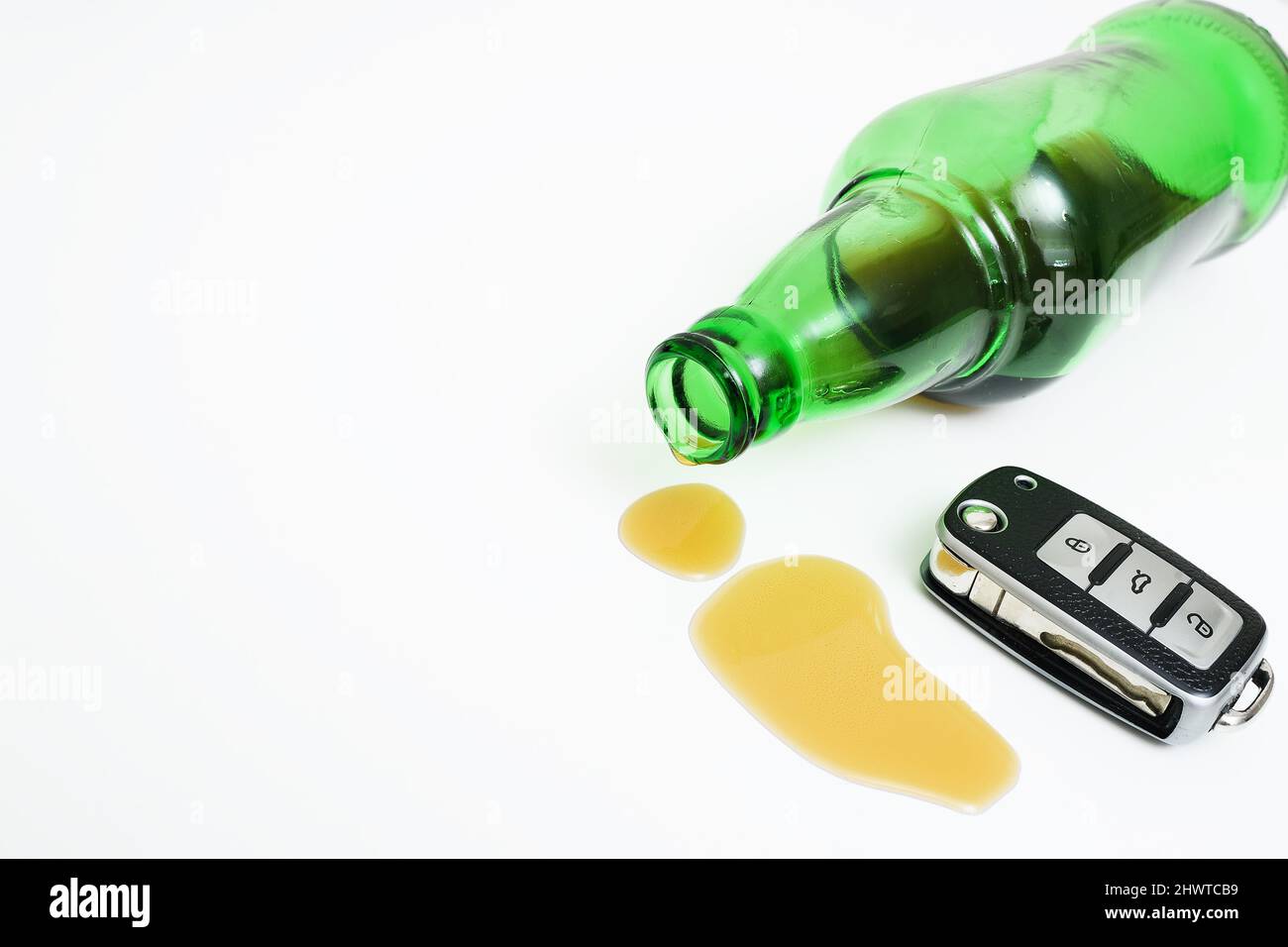 Grüne Glasflasche mit Alkohol- oder Bierresten und einem elektronischen Schlüssel auf weißem Hintergrund. Stockfoto