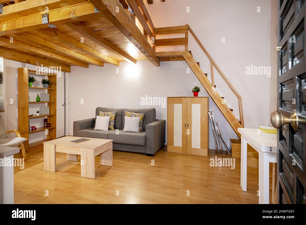 Zuhause mit hellem Holztisch, Schlafsofa in grauem Stoff gepolstert, passendem Holz Sideboard, Holzboden und Kiefernholztreppe Stockfoto