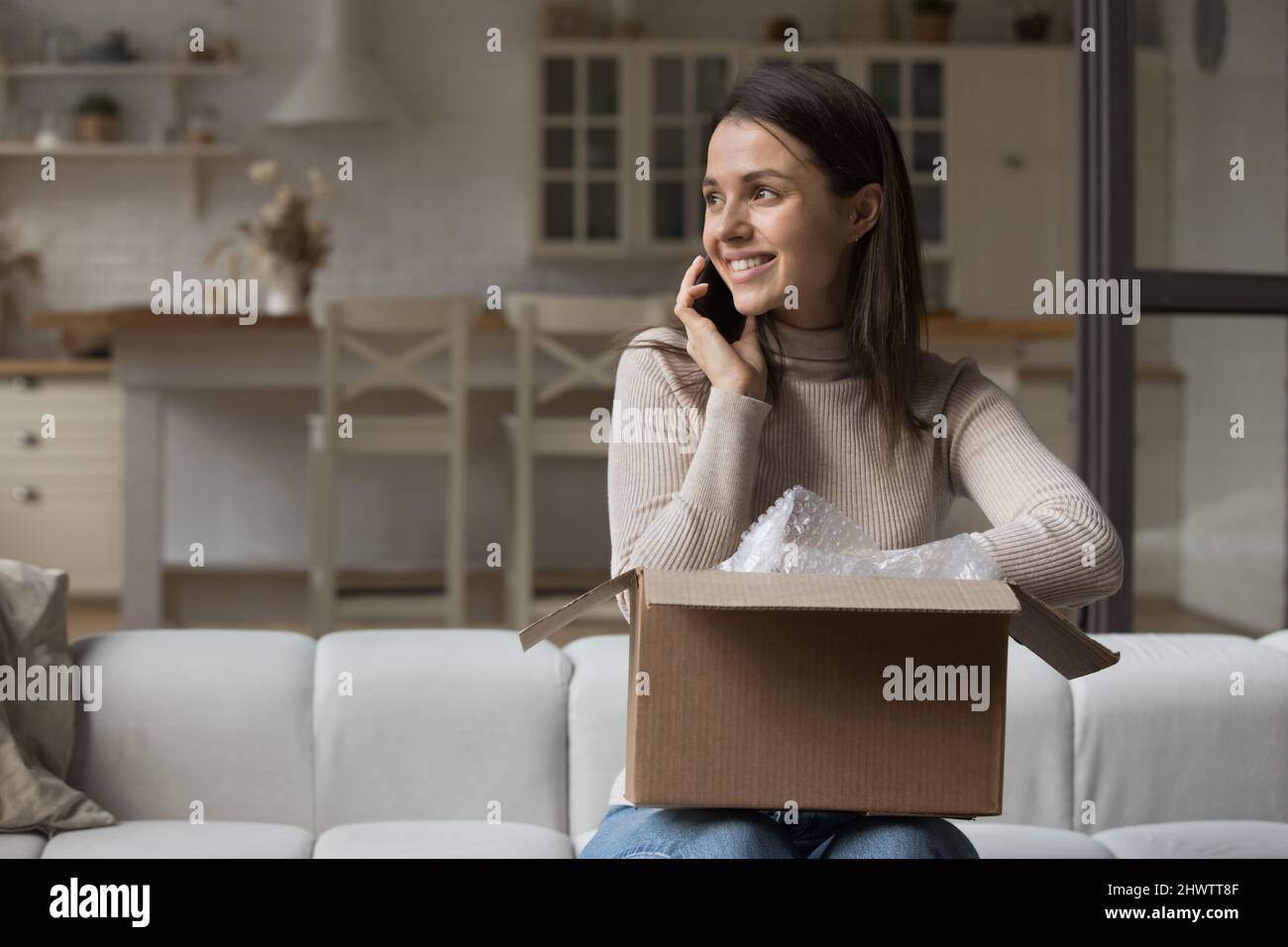 Frau im Gespräch auf dem Smartphone auf dem Sofa mit Paketkasten sitzend Stockfoto