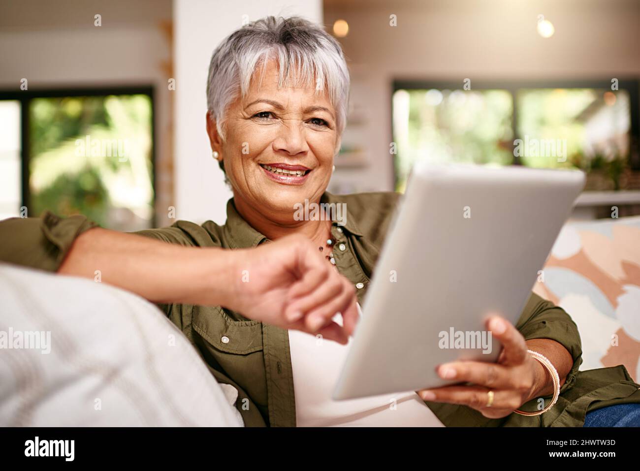 Jetzt habe ich mehr Zeit, meine Lieblingsfilme zu streamen. Porträt einer glücklichen älteren Frau, die sich zu Hause mit ihrem digitalen Tablet auf dem Sofa entspannt. Stockfoto