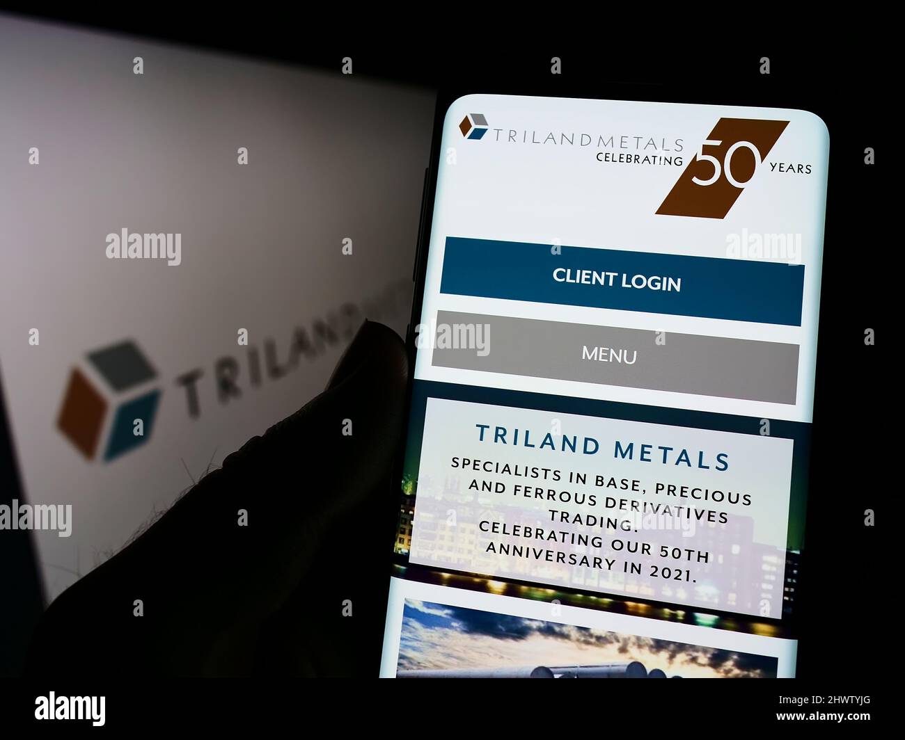 Person mit Smartphone und Website des britischen Unternehmens Triland Metals Limited auf dem Bildschirm vor dem Logo. Konzentrieren Sie sich auf die Mitte des Telefondisplays. Stockfoto