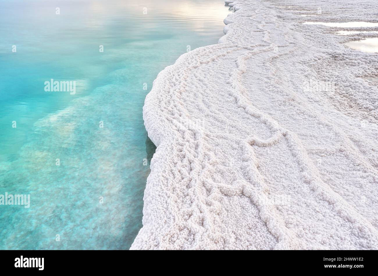 Morgensonne scheint auf weißen Salzkristallen, klares cyangrünes ruhiges Wasser in der Nähe, typische Landschaft am ein Bokek Strand, Israel Stockfoto