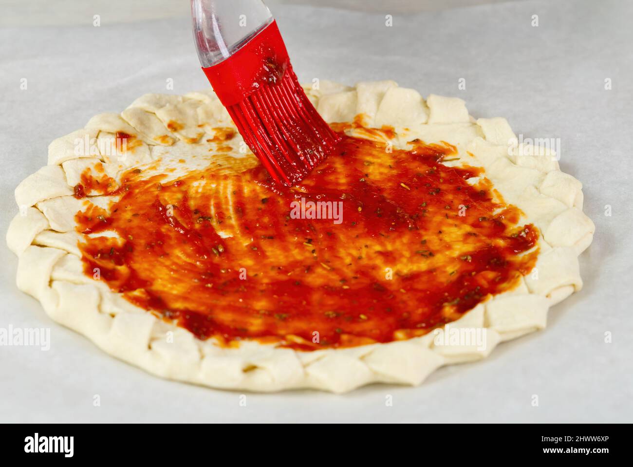 Pizzaherstellung. Draufsicht auf den Pizzateigboden mit einer geflochtenen Tortenkruste. Gebürstet mit Tomatenmark Stockfoto