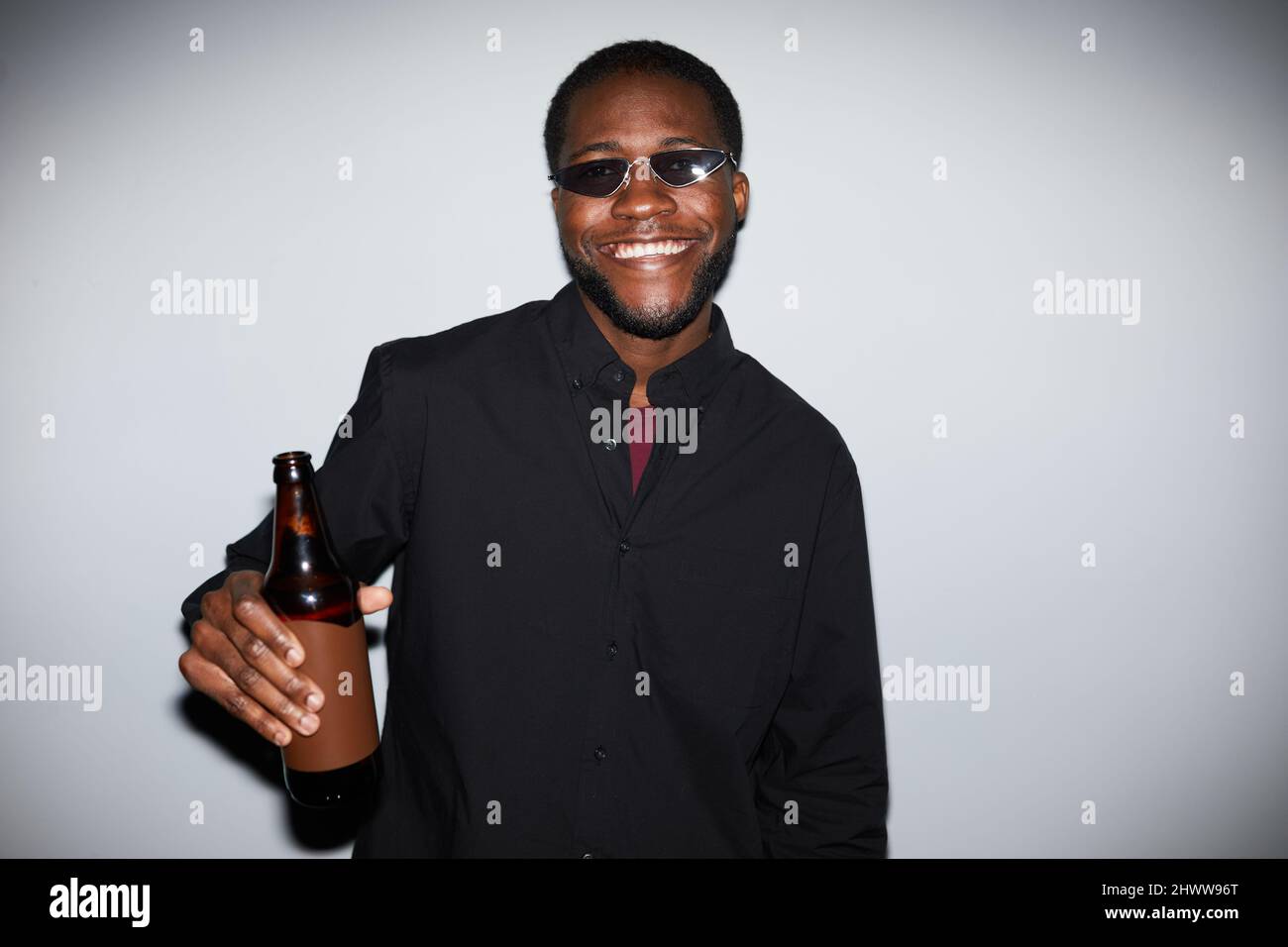 Minimal Taille up Porträt von sorglosen afroamerikanischen Mann Blick auf die Kamera bei der Party und hält einen Drink, mit Blitz aufgenommen Stockfoto
